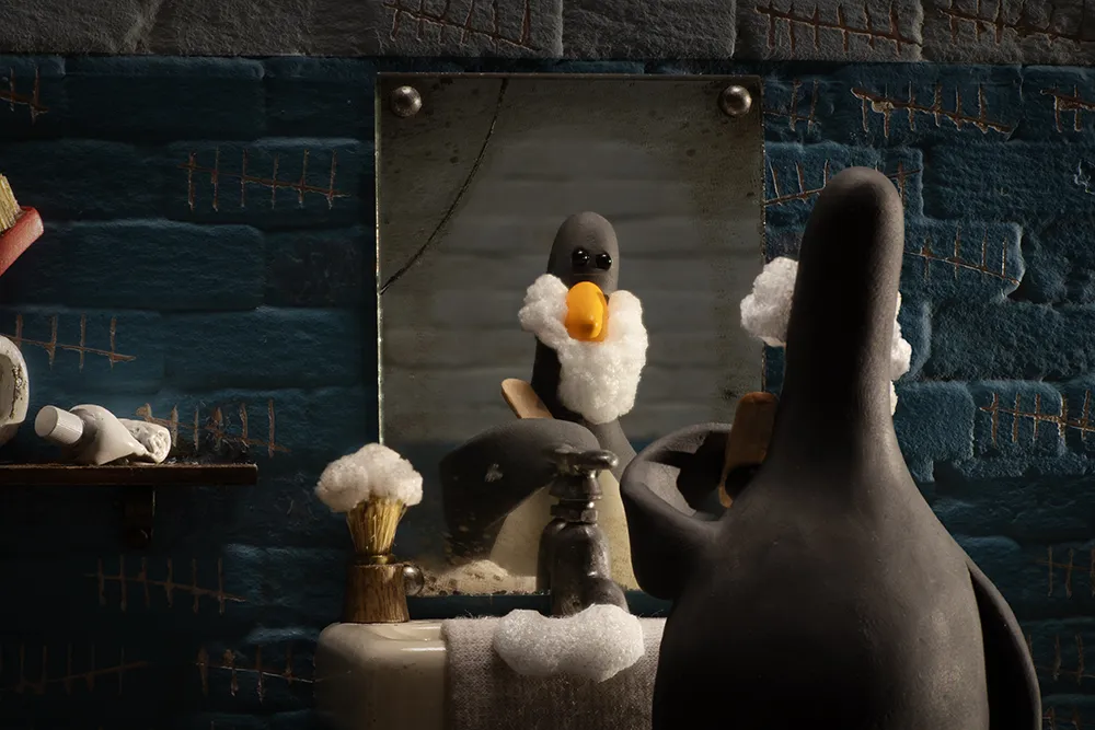 Cena da animação Wallace e Gromit: Avengança. O pinguim Feathers McGraw está fazendo sua barba na pia em frente a um espelho. Na pia de porcelana vemos um pincel de barbear coberto com espuma branca e uma toalha espuma branca. Na parede azul em que o espelho e a pia estão instalados, há vários riscos feitos para representar os dias que se passaram e uma prateleira na parte esquerda da tela com um tubo de espuma enrolado. Feathers passa uma lixa pelo rosto, tirando parte da espuma de seu rosto de pinguim.