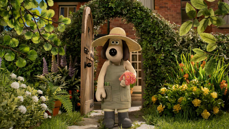 Cena da animação Wallace e Gromit: Avengança. Gromit está com um avental e um chapéu de palha olhando para seu jardim. Gromit é um cachorro da raça beagle com olheiras de abano escuras e pelo claro. Nos bolsos de seu avental verde desbotado há um par de tesouras verdes e ele segura na mão esquerda um par de luvas rosas com estampas floridas. Ele também usa botas pretas. Atrás dele vemos uma porta aberta em uma sebe e, atrás dela, uma casa de tijolos vermelhos fora de foco. Seu jardim é decorado por folhas verdes e flores brancas, lilases, amarelas e laranjas, crescendo em diferentes formatos.