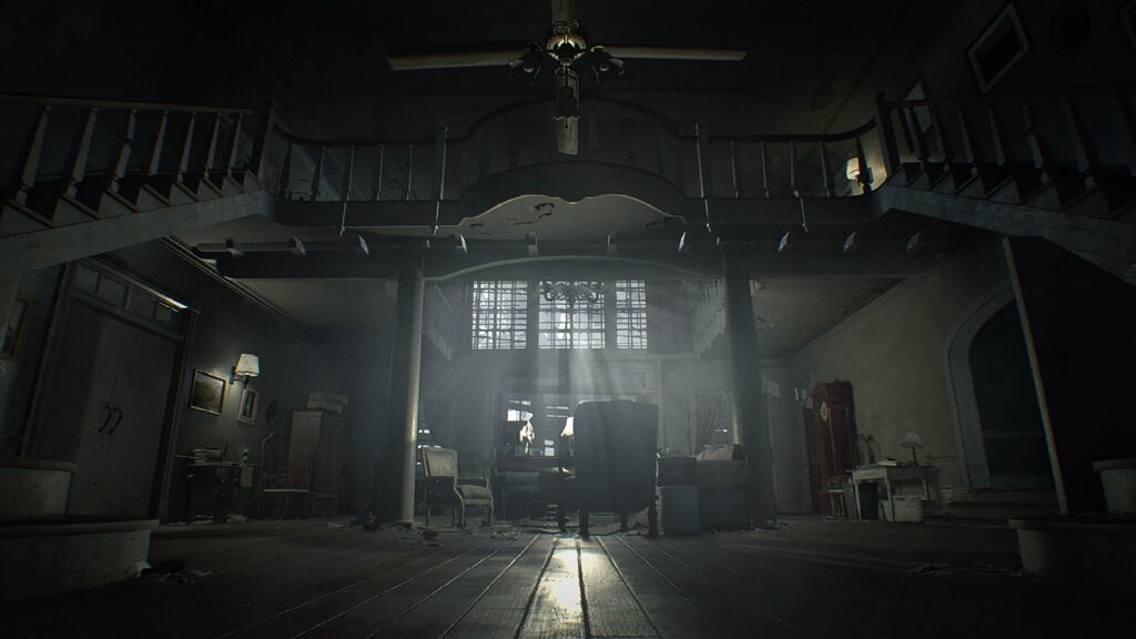 Cena do jogo Resident Evil 7: biohazard. Visão do saguão de entrada da residência Baker vinda de baixo para cima. Duas escadas nas laterais levam para os cômodos superiores, com uma ponte conectando-as e um ventilador parado no teto. No piso inferior, uma série de poltronas e caixas espalhadas pelo centro do cômodo. À esquerda, uma porta dupla branca com alguns quadros presos na parede à sua direita e um armário, iluminados por um abajur preso na parede. À direita, uma abertura na parede dá para outro cômodo, com uma escrivaninha branca e um relógio de coluna antigo à esquerda. Na parede oposta, as janelas estão bloqueadas por tábuas desorganizadas, impedindo que a luz entre uniformemente. Acima da entrada, outras janelas de vidro deixam mais da luz entrar, mas estão bloqueadas por sujeira.