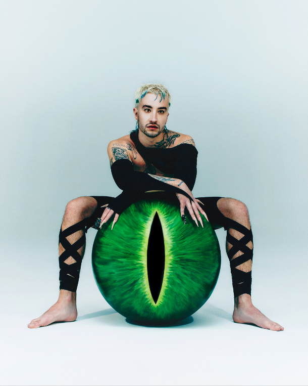 Nesta imagem, o cantor está centralizado sobre um fundo branco, vestido com um traje preto e com as pernas afastadas. Entre as pernas, há um globo ocular verde com uma íris típica de répteis, semelhante ao olho de um camaleão, em tons de verde, preto e amarelo. O cabelo de CHAMELEO está descolorido, com mechas verdes.