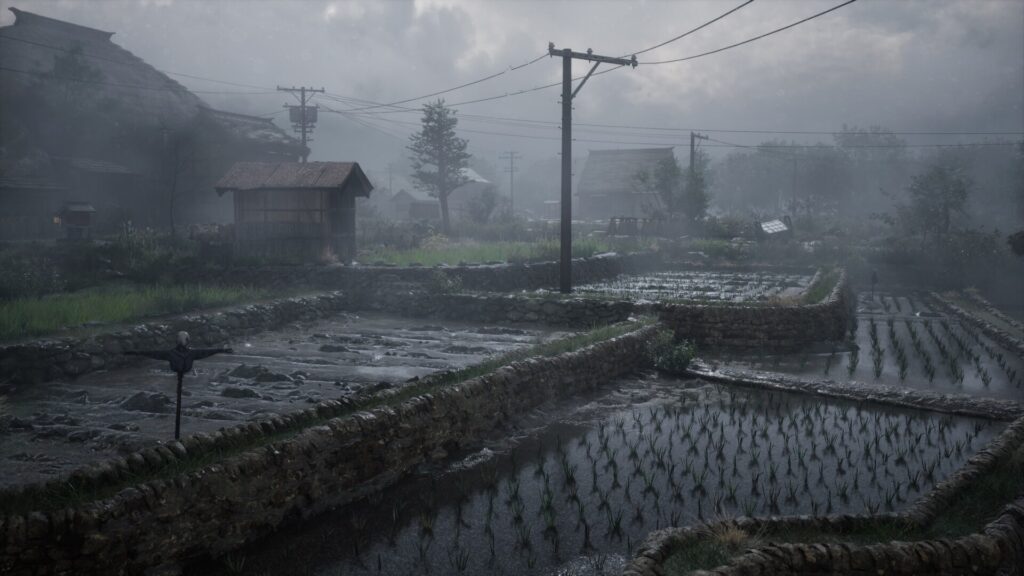 Cena do jogo Silent Hill f. Uma vista dos campos de plantação de Ebisugaoka, cobertos por uma névoa e sem nenhum habitante ao redor. Entre os pedaços de terra molhados, caminhos de terra elevados cortam o campo. No campo à esquerda, um espantalho de madeira com cara de pano está com os braços abertos. Uma linha telefônica corta o céu cinzento da paisagem, com um poste fincado no meio de um dos caminhos que cortam o campo, conectando com um outro poste mais atrás, à esquerda, e outro à direita, atrás da câmera. Uma pequena construção de madeira bloqueia a visão do poste à esquerda e, à distância, atrás do poste no centro, uma casa semi-oculta pela névoa. Algumas árvores se aparecem atrás da casa. Ao lado do poste à esquerda, atrás da construção de madeira, construções maiores aparecem, com telhados triangulares e feitos de palha.