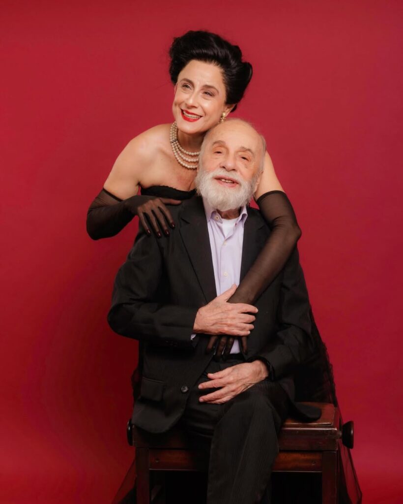 Fotografia da atriz Soraya Ravenle e do ator Renato Borghi. A imagem tem um fundo vermelho. Soraya está em pé, vestindo um figurino de Dalva de Oliveira. À frente, vemos Renato sentado, vestindo camisa e terno.