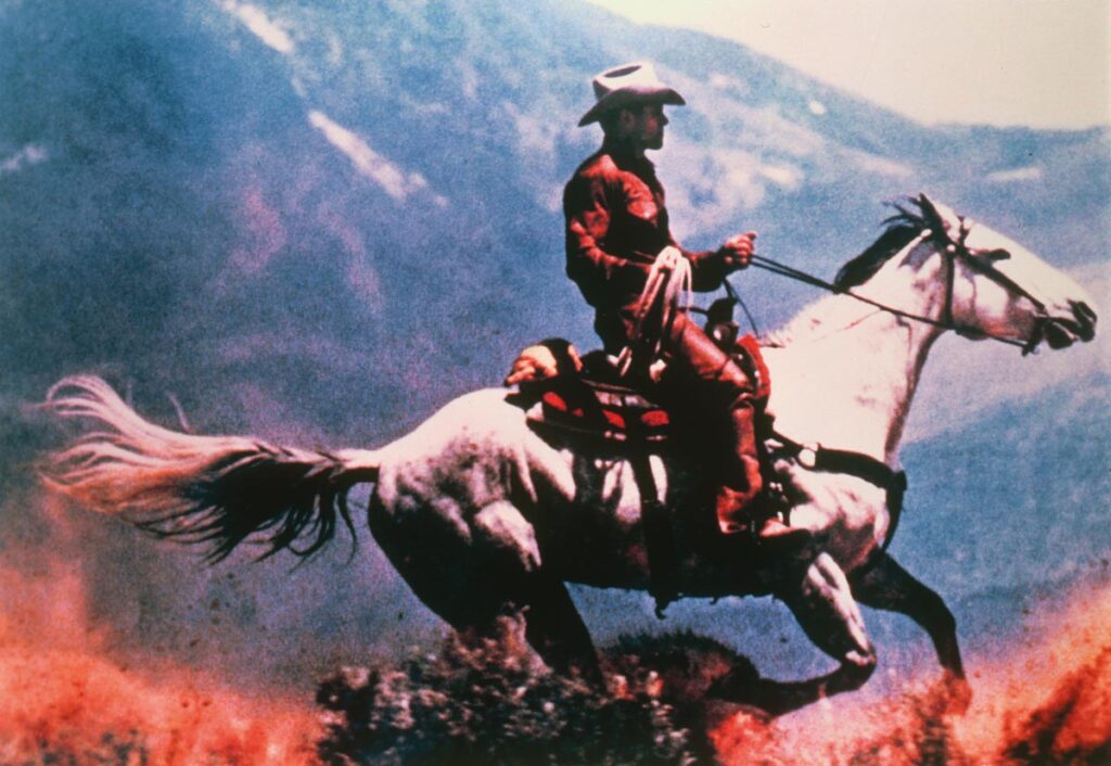 Imagem mostra um homem cavalgando. O cavalo é branco e o homem usa um chapéu, igualmente branco.